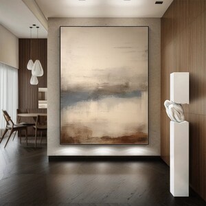 May include: Abstract painting in shades of brown, beige, and blue, hanging on a wall in a modern interior. The painting is framed in black and has a textured surface.