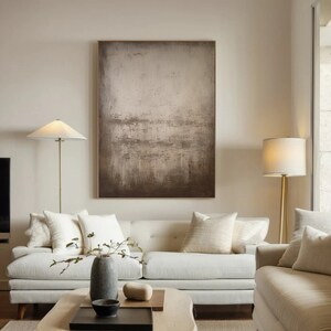 May include: A white sofa with multiple pillows sits in a living room with a large abstract painting on the wall, a floor lamp with a white shade, and a smaller floor lamp with a white shade.