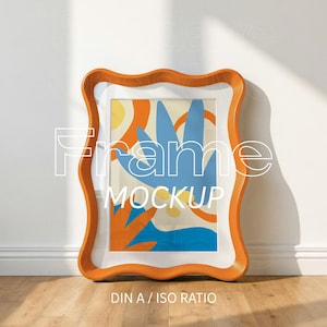May include: An orange wavy-edged picture frame containing an abstract print with blue, orange, and yellow shapes. The frame features the white text Frame MOCKUP and DIN A / ISO RATIO printed across the center and bottom of the image.