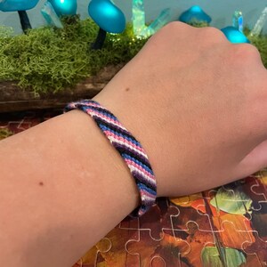 May include: A woven friendship bracelet with pink, blue, black and white stripes.