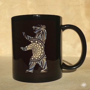 Puede incluir: Taza de cerámica negra con un contorno blanco de un oso con un diseño de mandala en oro y azul.