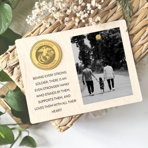 May include: A wooden plaque with a gold United States Marine Corps coin and a black and white photo of a family walking on a path. The plaque has the text "Behind every strong soldier, there is an even stronger family who stands by them, supports them, and loves them with all their heart!"