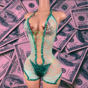May include: A light green fishnet bodysuit featuring a halter neckline, lace-up front detailing, and multicolored rhinestone embellishments on the chest. The garment includes a solid dark green fabric panel at the center and sides.