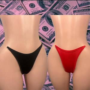 May include: Two thong-style underwear in black and red. The underwear are displayed on mannequins against a background of pink-tinted US one hundred dollar bills. The thongs have a simple, minimalist design.