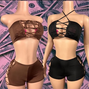 May include: Two matching sets of lingerie. One set is brown, the other is black. Each set includes a strapless top with a lace-up design and matching shorts with lace-up sides. The background is a pink and green pattern.