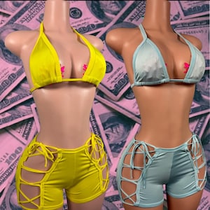 May include: Two sets of two-piece swimwear displayed on mannequins. One set is bright yellow, the other is light blue. Each set includes a triangle halter top and shorts with side lace-up detailing featuring multiple thin fabric ties.