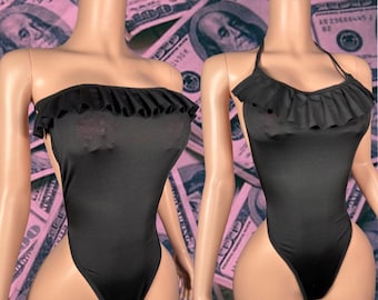 Puede incluir: Dos trajes de baño negros de una pieza con ribete de volantes. Un traje de baño tiene cuello halter y el otro tiene un escote sin tirantes.