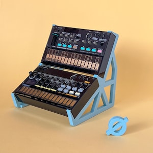 May include: A blue, triangular stand holds two black electronic music synthesizers. The top synthesizer is a KORG volca fm, and the bottom synthesizer is a KORG volca sample.