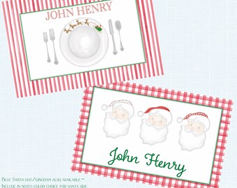 May include: Two Christmas-themed place cards. One features a plate setting with silverware and the name "JOHN HENRY". The other has three Santa faces and the name "John Henry". Both have red and green accents.