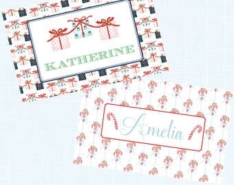 May include: Two Christmas-themed name cards. One card features a pattern of gift boxes and the name "KATHERINE" in green. The other card has a pattern of candy canes and the name "Amelia" in blue.