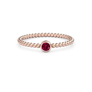 May include: Rose gold ring with a beaded band and a round, deep red gemstone center. The ring is set against a white background, highlighting the delicate design and the vibrant color of the gemstone.