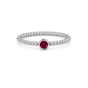 May include: A silver ring with a beaded band and a round, deep red gemstone at the center. The gemstone is set in a bezel setting, and the ring is displayed against a white background.