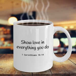 Peut inclure: Une tasse à café en céramique blanche avec du texte noir qui dit "Show love in everything you do 1 Corinthians 16:14".