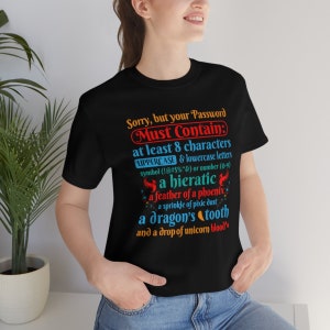 May include: A black t-shirt with a humorous message about password requirements. The text reads "Sorry, but your Password Must Contain: at least 8 characters UPPERCASE & lowercase letters symbol (!@#$%^&) or number (0-9) a hieratic a feather of a phoenix a sprinkle of pixie dust a dragon's tooth and a drop of unicorn blood."