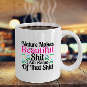 Könnte beinhalten: Eine weiße Keramik-Kaffeetasse mit schwarzem Henkel. Die Tasse hat ein buntes Design mit dem Text "Nature Makes Beautiful Shit I Am Some Of That Shit!"