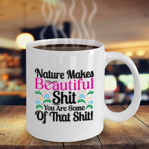 Könnte beinhalten: Eine weiße Keramik-Kaffeetasse mit schwarzem Henkel. Die Tasse hat ein schwarzes und pinkfarbenes Design mit dem Text "Nature Makes Beautiful Shit You Are Some Of That Shit!"