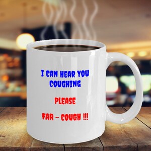 May include: White ceramic coffee mug with the text "I can hear you coughing. Please far-cough!!!" in blue and red lettering.