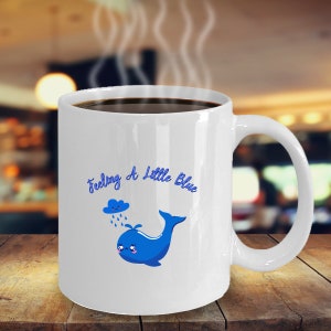 May include: White ceramic coffee mug with a blue whale and a blue cloud with raindrops. The text "Feeling A Little Blue" is written in blue cursive.