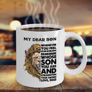 Può includere: Una tazza da caffè in ceramica bianca con una grafica di leone nero e il testo "My Dear Son Whenever You Feel Overwhelmed Remember Whose Son You Are And Straighten Your Crown Love, Dad".