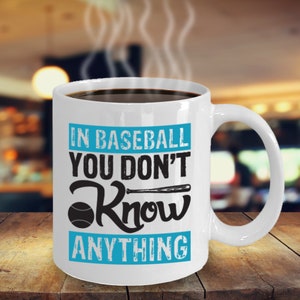 May include: White ceramic coffee mug with a blue and black design. The mug has the text "In baseball you don't know anything" with a baseball and bat graphic.