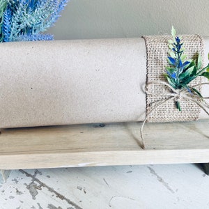 May include: A brown paper-wrapped gift box with a burlap bow and blue and green floral accents. The box is sitting on a wooden stand.