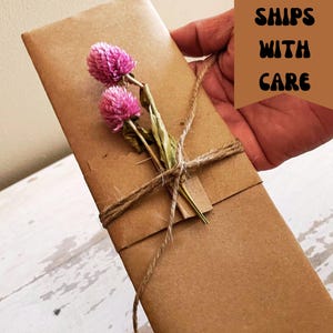 May include: A brown paper package tied with twine and decorated with dried pink flowers. The package is labeled "SHIPS WITH CARE".