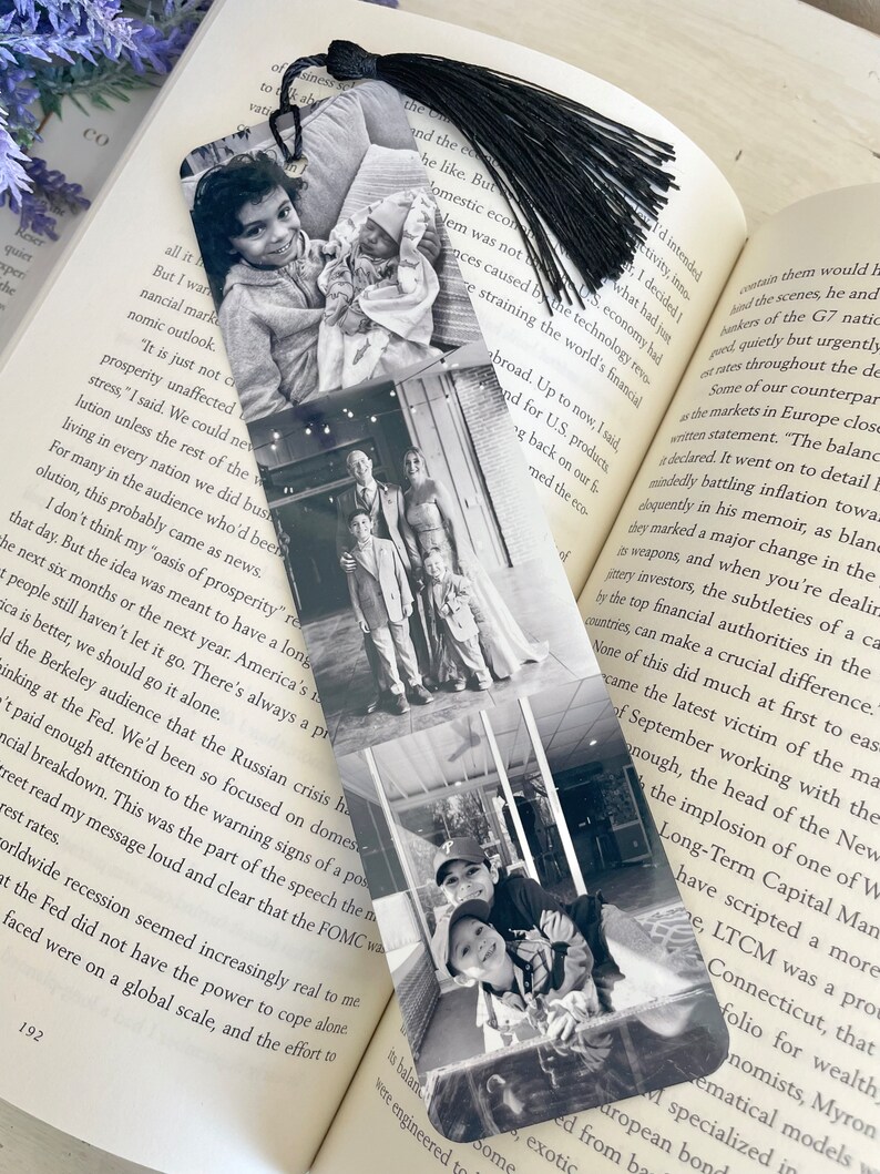 May include: Black and white photo bookmark with a tassel. The bookmark features a collage of family photos. The bookmark is on top of an open book with text about the economy.