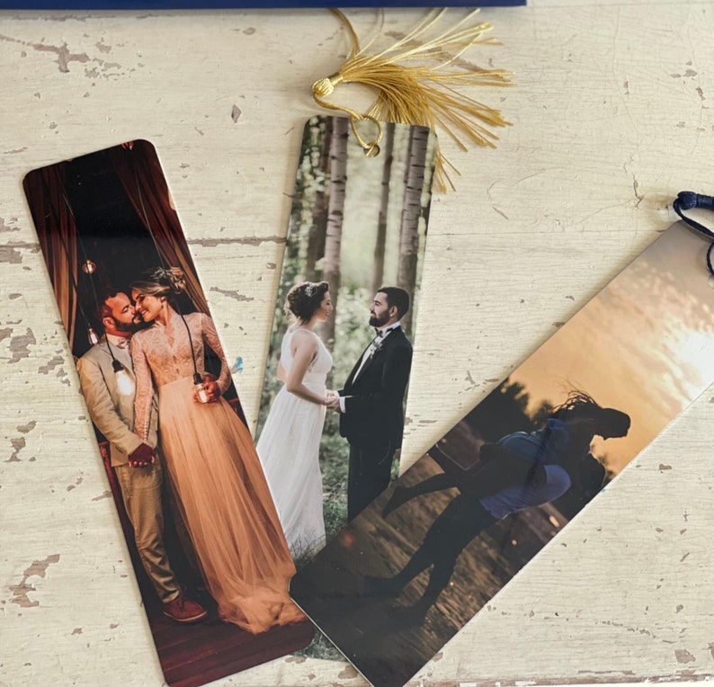 May include: Three personalized bookmarks featuring photographs of couples. The bookmarks are printed on a white background with a gold tassel.