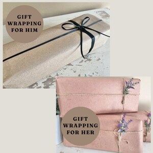 May include: Two gift boxes wrapped in brown paper. The top box is tied with a black ribbon and the bottom box is tied with twine and decorated with dried lavender sprigs. The text "GIFT WRAPPING FOR HER" is printed on a circle sticker on the bottom box.