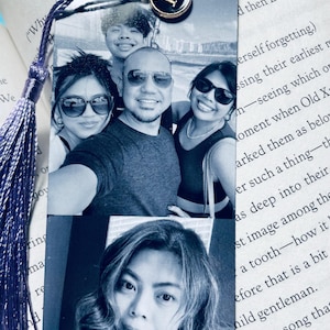 May include: A purple tassel bookmark with a metal charm featuring the letter K. The bookmark has two photos of a family. The top photo shows a family of four, and the bottom photo shows a woman with long dark hair.