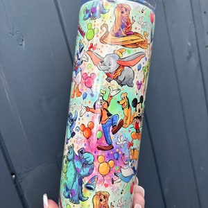 May include: A stainless steel tumbler with a colourful design featuring various Disney characters, including Mickey Mouse, Minnie Mouse, Donald Duck, Goofy, Pluto, Dumbo, Stitch, and Rapunzel. The tumbler is decorated with confetti, balloons, and fireworks.
