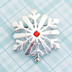 May include: Silver snowflake brooch with a red rhinestone in the center.