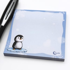 Könnte beinhalten: Ein quadratischer Notizblock mit hellblauem Rand und einer Cartoon-Pinguin-Illustration. Der Pinguin ist schwarz und weiß und steht auf einer kleinen Eisscholle. Auf dem Notizblock steht das Wort "Kyashi" unten rechts.