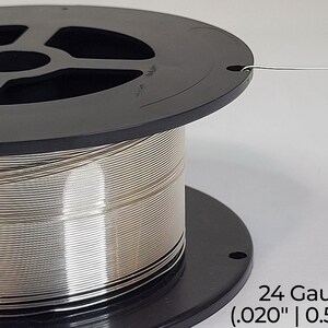 Pode incluir: Uma bobina de fio prateado de calibre 24, com 0,51 mm de di&acirc;metro (0,020 polegadas). O fio est&aacute; enrolado em torno de uma bobina de pl&aacute;stico preto.