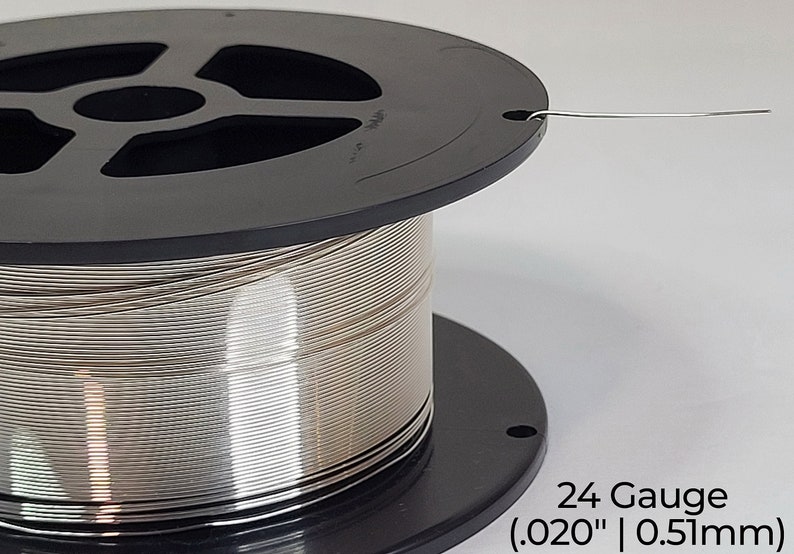 Pode incluir: Uma bobina de fio prateado de calibre 24, com 0,51 mm de di&acirc;metro (0,020 polegadas). O fio est&aacute; enrolado em torno de uma bobina de pl&aacute;stico preto.