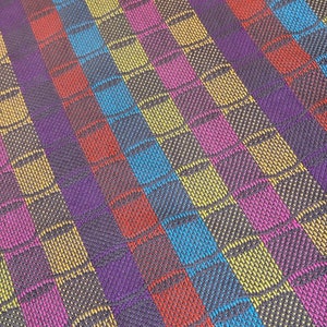 May include: Multicolored striped fabric with a woven pattern of small squares and circles. The fabric is made of a soft, textured material and features a variety of colors, including purple, blue, yellow, pink, and red.