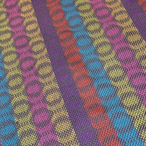 May include: A close-up of a colourful striped fabric with a textured pattern. The fabric is made of woven threads in shades of yellow, pink, blue, red, and purple.