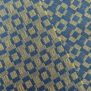 May include: Close-up of a blue and yellow fabric with a repeating geometric pattern. The pattern is made up of small squares and rectangles.