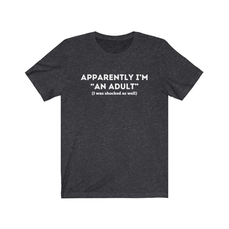 May include: A dark heather grey t-shirt with the text "Apparently I'm "An Adult" (I was shocked as well)" printed in white.