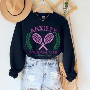 May include: Black sweatshirt with a pink and green graphic that says "Anxiety Antisocial Club Members Only" with two pink tennis rackets crossed over each other.