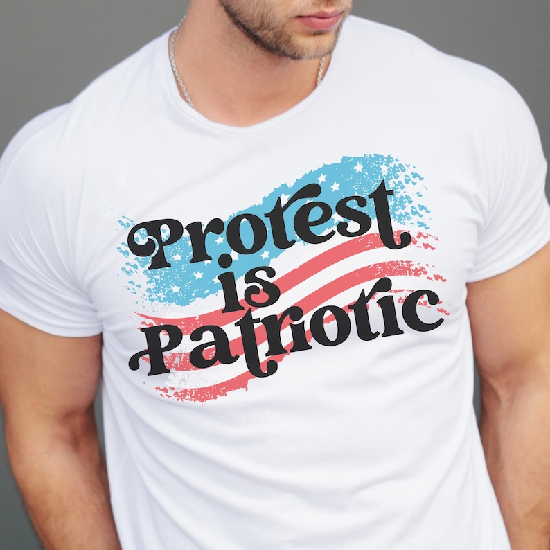 Puede incluir: Camiseta blanca con un dise&ntilde;o de bandera americana roja, blanca y azul y el texto "Protest is Patriotic" en negro.