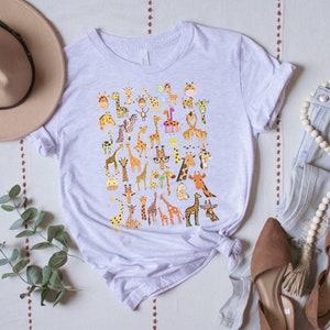 Pu&ograve; includere: Una maglietta grigia chiaro con una stampa grafica di diverse giraffe in pose e colori diversi. Le giraffe indossano tutte accessori diversi, come cappelli, occhiali e sciarpe.