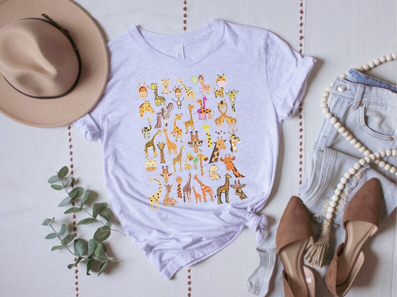 Pu&ograve; includere: Una maglietta grigia chiaro con una stampa grafica di diverse giraffe in pose e colori diversi. Le giraffe indossano tutte accessori diversi, come cappelli, occhiali e sciarpe.
