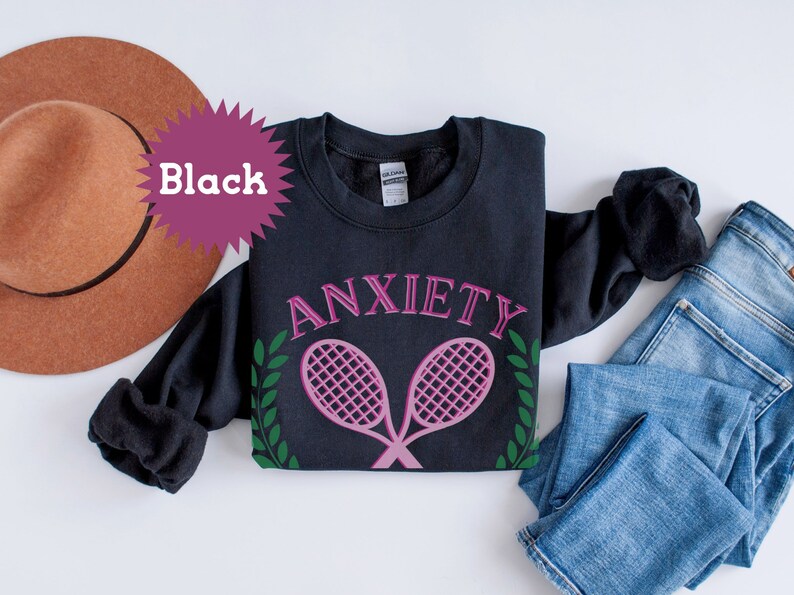 May include: Black sweatshirt with the text "ANXIETY" in pink lettering and two pink tennis rackets with green leaves on either side.
