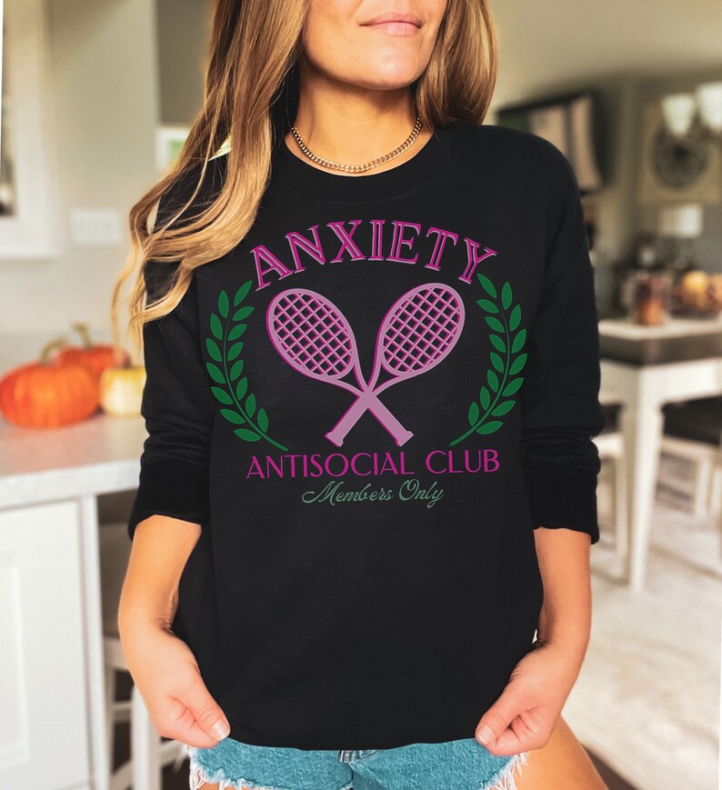 May include: Black sweatshirt with a pink graphic of two crossed tennis rackets with green laurel wreaths and the text "Anxiety Antisocial Club Members Only".