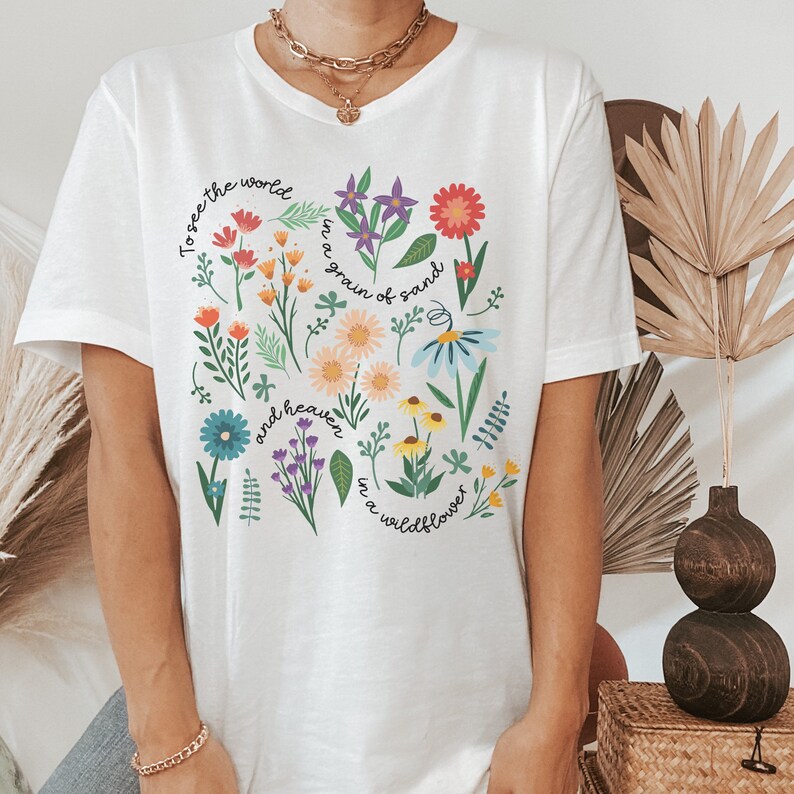 May include: White t-shirt with a floral design and the text "To see the world in a grain of sand and heaven in a wildflower."