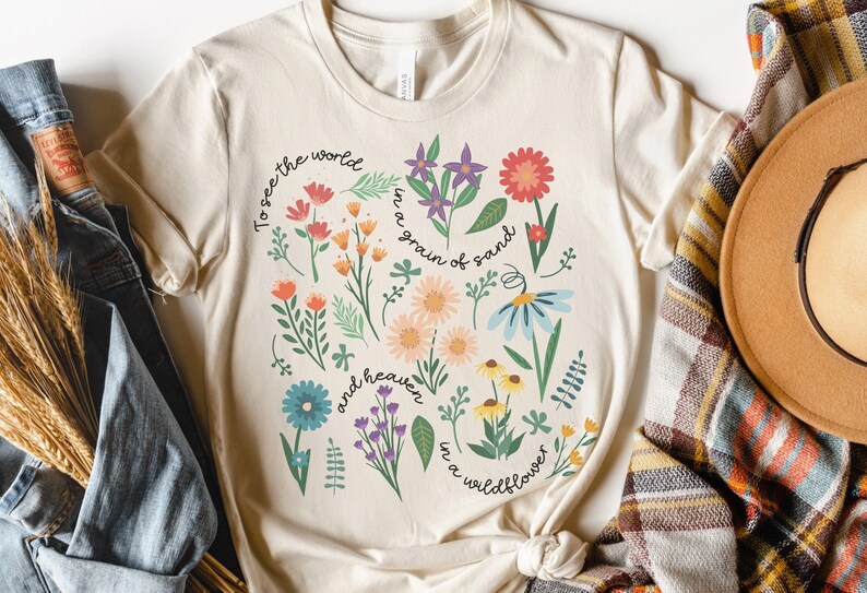 May include: A beige t-shirt with a floral design and the text "To see the world in a grain of sand and heaven in a wildflower".