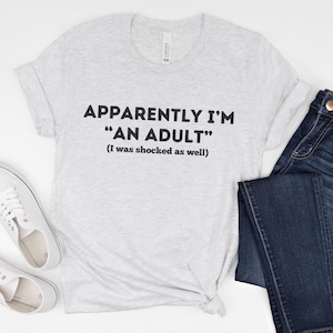 May include: Gray t-shirt with the text "Apparently I'm "An Adult" (I was shocked as well)"