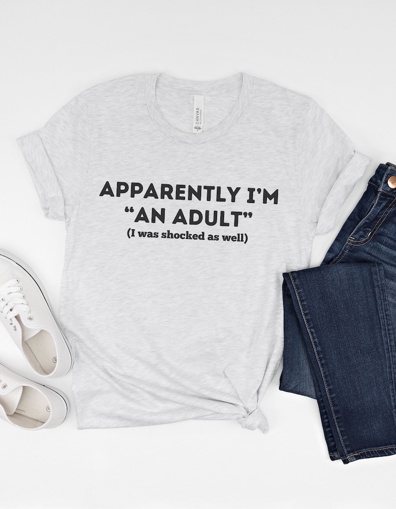 May include: Gray t-shirt with the text "Apparently I'm "An Adult" (I was shocked as well)"