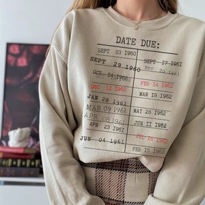 May include: A beige sweatshirt with a graphic of a date due list. The list includes dates from September 1960 to February 1963.